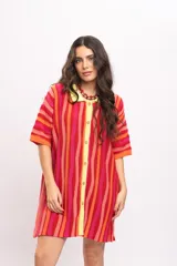 Vestido camisola corto de tejido fresco de algodón, con diseño a rayas verticales en tonos rojos, naranjas y fucsias. Cuenta con cuello polo y botonadura frontal en tono amarillo claro, y mangas cortas holgadas.