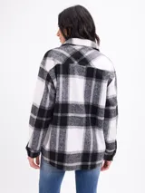 Sobrecamisa de franela con estampado de cuadros grandes en tonos blanco y negro. Presenta cuello camisero, cierre frontal con botones, mangas largas con puños abotonados y bolsillos frontales con solapa.