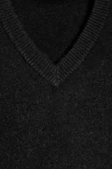 Jersey de punto negro, con cuello en V (pico) y manga larga, acabado en rib en puños, cuello y bajo.