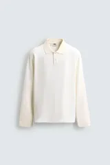Polo de manga larga color blanco roto, confeccionado en algodón con estructura piqué. Presenta cuello solapa con cierre de botones y aberturas laterales en el bajo.