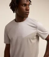 Remera deportiva de hombre, color gris claro, con cuello redondo y manga corta. Presenta un sutil efecto degradado o panel de color más claro en la zona del pecho.