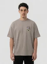 Remera de algodón color gris topo con corte relajado. Presenta un diseño gráfico estampado en la espalda que combina una figura abstracta con parlantes en tonos violeta y verde ácido.