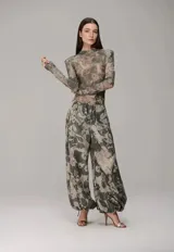 Pantalón de corte holgado con estampado camuflado en tonos verdes y beige. Presenta cintura elástica con cordón ajustable y puños inferiores también ajustables con cordón, permitiendo modificar su silueta.