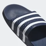 Chancletas Adidas Adilette de color azul marino, con tira superior texturizada y las tres bandas características de la marca en color blanco. Cuentan con una plantilla anatómica moldeada para mayor confort.
