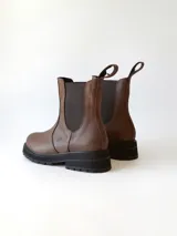 Bota tipo Chelsea de cuero color chocolate, con paneles elásticos laterales, tirador trasero y suela track negra de goma.