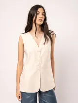 Chaleco color crema de lino con corte sastrero, largo a la cadera, forro interno, botones delanteros, silueta levemente entallada y tajo cruzado en la espalda.
