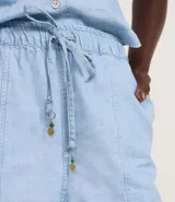 Short estilo runner de jeans azul claro, con cintura elástica y lazo ajustable. Presenta bolsillos carpinteros y un colgante de piña en el lazo.