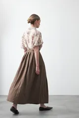 Falda larga plisada color marrón, de silueta amplia y caída fluida.