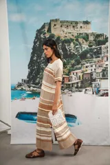 Vestido largo de tejido calado con rayas horizontales en tonos beige, marrón y amarillo. Tiene corte recto, hombros caídos, tajo lateral y logo bordado en la manga.