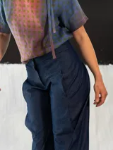 Pantalón babucha de denim azul, con corte a la cintura baja y diseño tipo origami. Presenta pliegues y costuras que favorecen la silueta. Creado y producido en Uruguay.