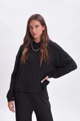 Hoodie de tela rib negra con capucha, de corte holgado y mangas largas con puños ajustados.