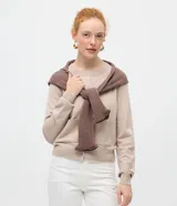 Cardigan de punto color beige, de corte clásico y manga larga, con cuello redondo, cierre frontal por botones y bolsillos delanteros funcionales.