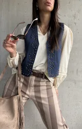 Chaleco de jean oscuro con tachas doradas aplicadas en la parte frontal y escote en V.