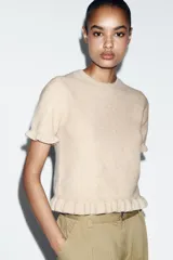 Jersey de punto de cuello redondo y manga corta, con detalle de volantes en el ruedo y en los puños.