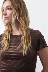 Top de manga corta confeccionado en terciopelo negro, con textura acanalada y acabado con leve brillo. Presenta un diseño ajustado al cuerpo con cuello redondo.