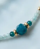 Collar de acero con baño de oro, compuesto por una delicada cadena de pequeñas cuentas en tonos celestes y verdes, intercaladas con piedras naturales redondas de mayor tamaño en color turquesa y verde oscuro.