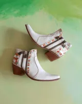 Botas cortas de cuero blanco pintadas a mano de Carolina De Cunto, con taco cuadrado de madera, doble cierre lateral y detalles geométricos multicolores.