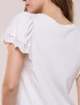 Remera blanca semi entallada de algodón con elastano, escote redondo y mangas cortas estilo tulipán confeccionadas en broderie calado con bordados florales y terminación festonada.