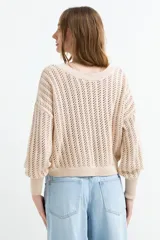 Sweater de tejido calado color beige, con escote en V y mangas largas holgadas con puños ajustados.