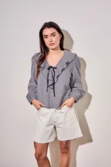 Blusa de corte oversize con estampado de cuadros vichy en blanco y negro. Presenta un cuello con volados, mangas largas con puños elásticos y un cierre frontal con lazo negro.