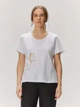 Remera de manga corta color blanco, confeccionada en algodón con spandex, con escote redondo y detalle de delicado bordado floral en el lateral inferior.