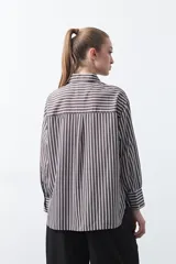 Camisa a rayas verticales blancas y marrones, de manga larga con puños abotonados, cuello camisero y botones frontales. Incluye un bolsillo en el pecho con bordado sutil.