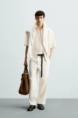 Pantalón de calce relajado confeccionado en tejido de viscosa y yute color tostado. Presenta cintura elástica ajustable con cordón, bolsillos laterales, bolsillos traseros de vivo y cierre frontal con cremallera y botón.