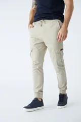 Pantalón cargo color verde oliva, de corte slim, con cintura elastizada y cordón ajustable. Presenta bolsillos laterales tipo cargo con botones y puños elásticos en los tobillos.