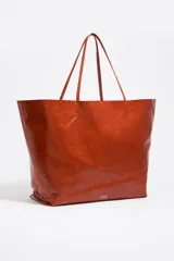 Bolso shopper de estructura blanda confeccionado en piel vacuna con acabado brillante. Cuenta con doble asa de hombro, costura central vertical y logo metálico de la marca en la base frontal.