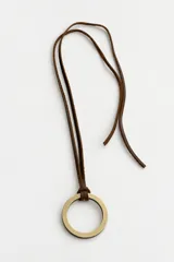 Collar largo de diseño artesanal con cordón de cuero en color chocolate y un dije circular metálico en tono dorado envejecido.