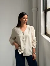 Blusa de lino color beige con cuello en V, cierre frontal con botones y mangas largas con sutil fruncido en los hombros.