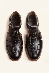 Sandalias de cuero color marrón, tipo romanas, con talón cerrado, tira en T con detalles de tachas metálicas, aberturas laterales y cierre de hebilla ajustable. Tienen tacón bajo de madera.
