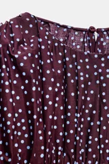Blusa de color bordó con estampado de lunares claros, confeccionada con cuerpo en nido de abeja elástico, cuello redondo y mangas abullonadas por debajo del codo.