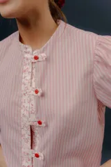Blusa de algodón a rayas rosadas y blancas, con mangas cortas abullonadas, cuello mao y detalles de tela estampada floral en la botonera y los puños.