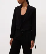 Blazer corto de sastre de la marca Cortelle, color negro, confeccionado en poliéster. Cuenta con cuello con solapa, mangas largas con amarre en los puños, bolsillos delanteros y cierre frontal por cordón ajustable con punteras metálicas.