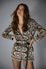 Saco sastrero con escote en V y mangas largas, confeccionado en gabardina liviana negra con bordados florales y patrones geométricos en tonos beige, dorado y toques de color (fucsia, verde, violeta). Presenta botones ocultos, bolsillos ojal, hombreras y un cinturón fino de cuero negro.