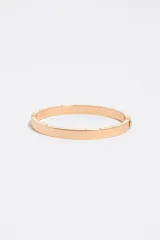 Pulsera rígida de metal dorado con detalles de esmalte negro en el borde y letras grabadas a lo largo de la pieza. Cuenta con cierre de bisagra.
