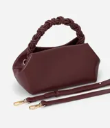 Bolso de mano pequeño color borgoña, con cuerpo de forma trapezoidal y asas cortas trenzadas. El material parece ser cuero sintético (PU).