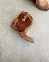 Botas texanas cortas de cuero vacuno color marrón con detalles de cuero marrón oscuro y tachas plateadas.