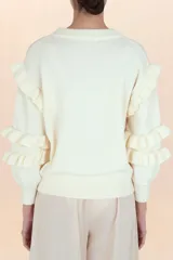 Suéter de punto color blanco, con cuello redondo, mangas largas abullonadas y detalle de volantes en los hombros y antebrazos.