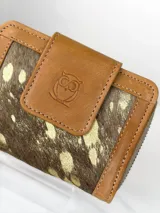 Mini billetera de cuero marrón con solapa frontal que presenta un grabado de un búho. El cuerpo de la billetera está confeccionado en cuero con pelo natural en tonos marrones y manchas doradas.