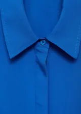 Camisa de corte recto y diseño largo, confeccionada en tejido fluido mezcla de lyocell y lino. Presenta cuello camisero, cierre frontal de botones ocultos bajo tapeta, mangas largas con puños abotonados y dos bolsillos de solapa en el frente.
