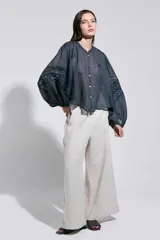 Camisa azul semitransparente con mangas abullonadas estilo globo, cuello redondo y cierre frontal con botones. Presenta detalles de encaje calado en las mangas.