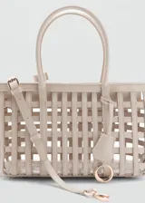 Bolso cesta de diseño trenzado en color beige, con dos asas cortas de mano y un asa larga ajustable y desmontable. Incluye detalle de charm colgante y herrajes metálicos.