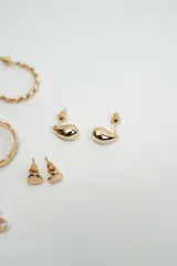 Set de aros variados en tono dorado, que incluye aros tipo argolla trenzados, argollas lisas, aros tipo gota, aros con piedras brillantes, aros con perlas y aros con diseño floral.
