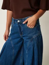 Jean de denim azul de tiro medio, con diseño wide leg de corte muy amplio y pinzas laterales decorativas que aportan volumen.