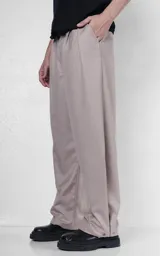Pantalón sastrero de corte oversize en color beige, con pinzas frontales profundas que aportan volumen y movimiento. Presenta cintura ancha, bolsillos laterales y bolsillos tipo ojal en la parte trasera, con detalle de botones en el ruedo.