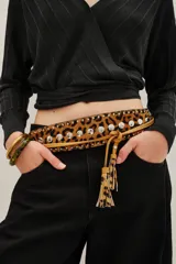 Cinturón tipo faja de cuero vacuno con estampado animal print, decorado con tachas metálicas plateadas y tiras laterales con borlas decorativas.