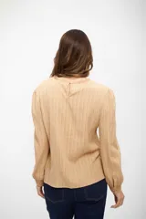 Blusa de color beige con textura acanalada, manga larga con puños ajustados y detalle de encaje vertical en el frente.