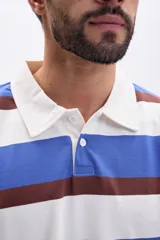 Remera de manga larga tipo polo con cuello camisero y cierre frontal de botones. Presenta un diseño de rayas horizontales anchas en tonos azul, blanco y marrón.